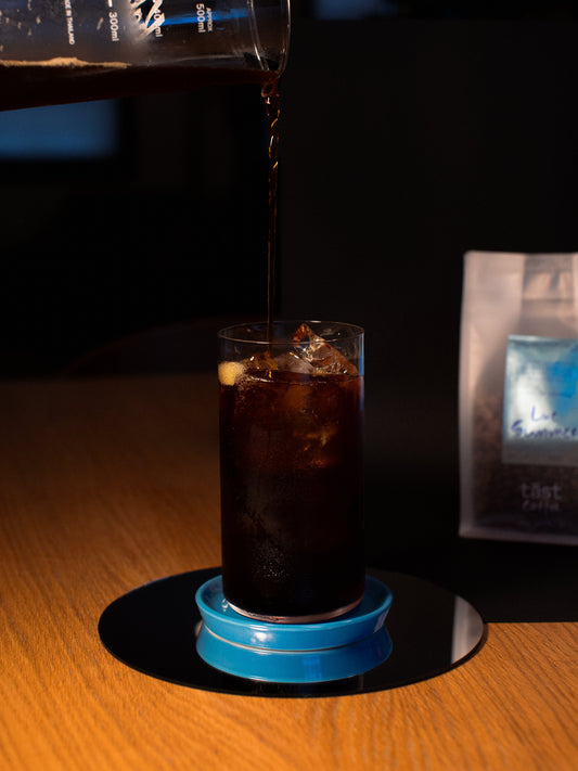 Tall drinking glass full of ice and coffee while coffee is being poured from a carafe above