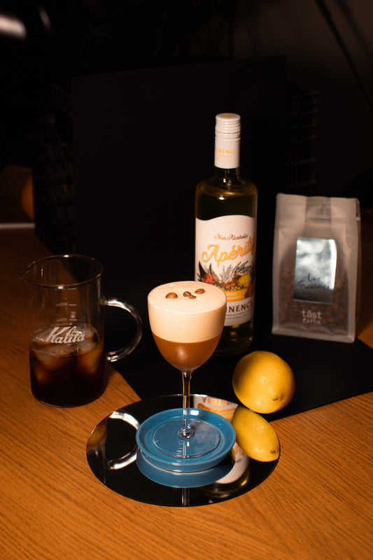 brown cocktail in a coupe glass with large foam head and three coffee beans perched on top