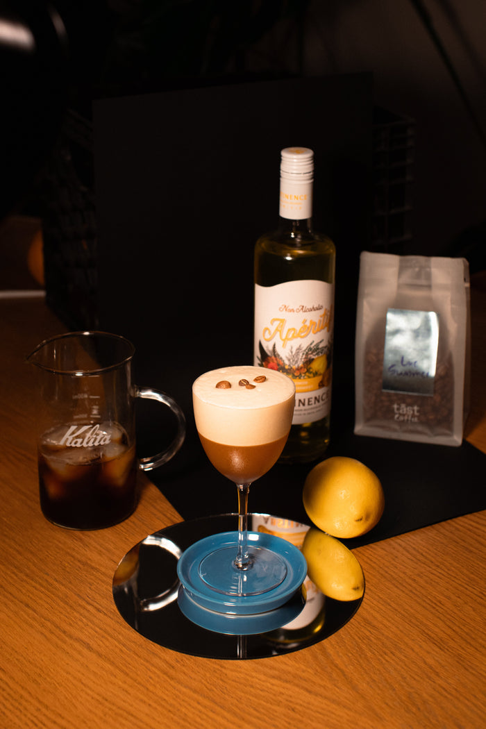 brown cocktail in a coupe glass with large foam head and three coffee beans perched on top